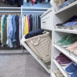 Shoes placed on shelves, drawer pulled out showing clothing hamper and shirts hung on racks in background