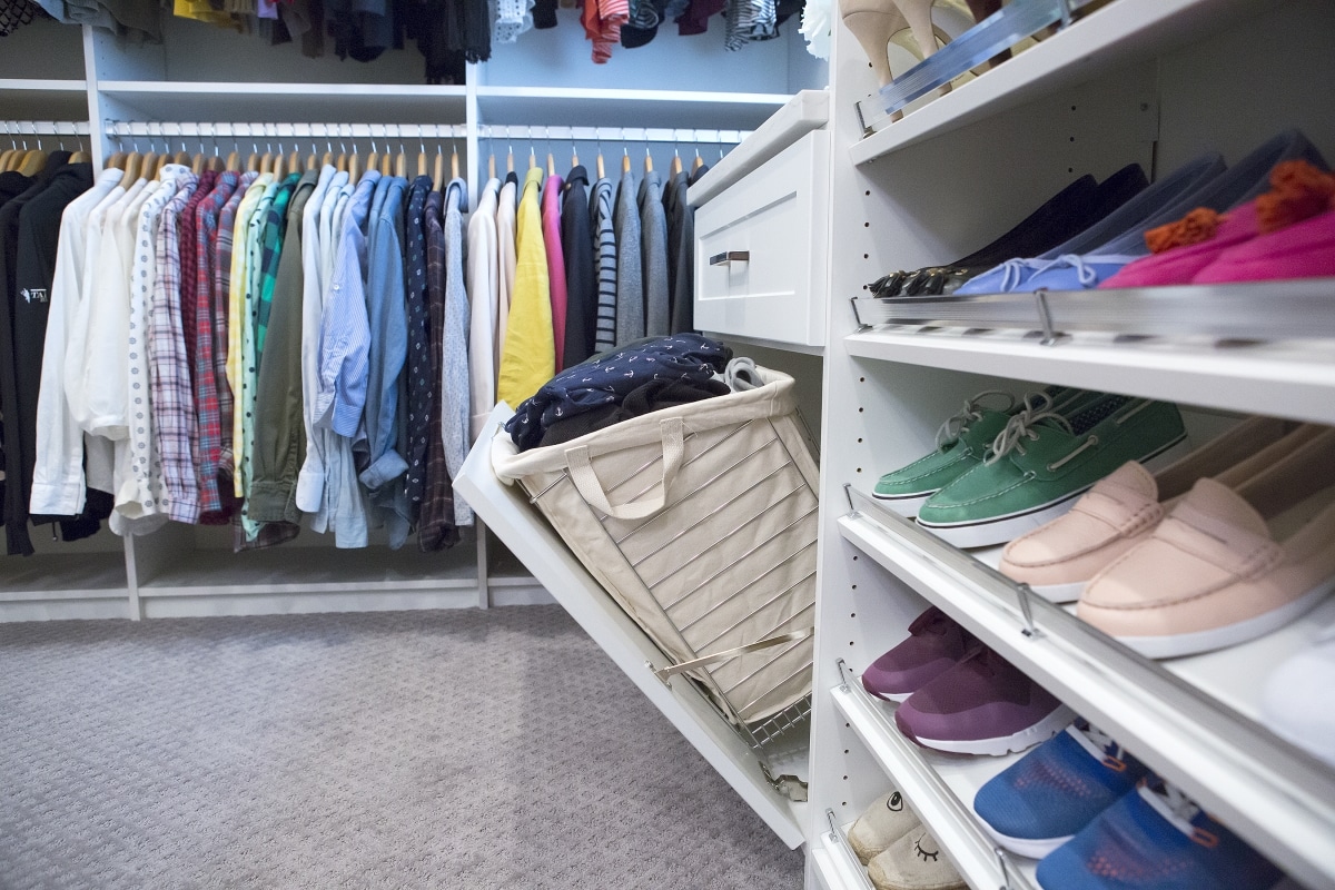 Shoes placed on shelves, drawer pulled out showing clothing hamper and shirts hung on racks in background