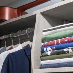 Shirts folded on shelves and hanging on racks with guitar on top