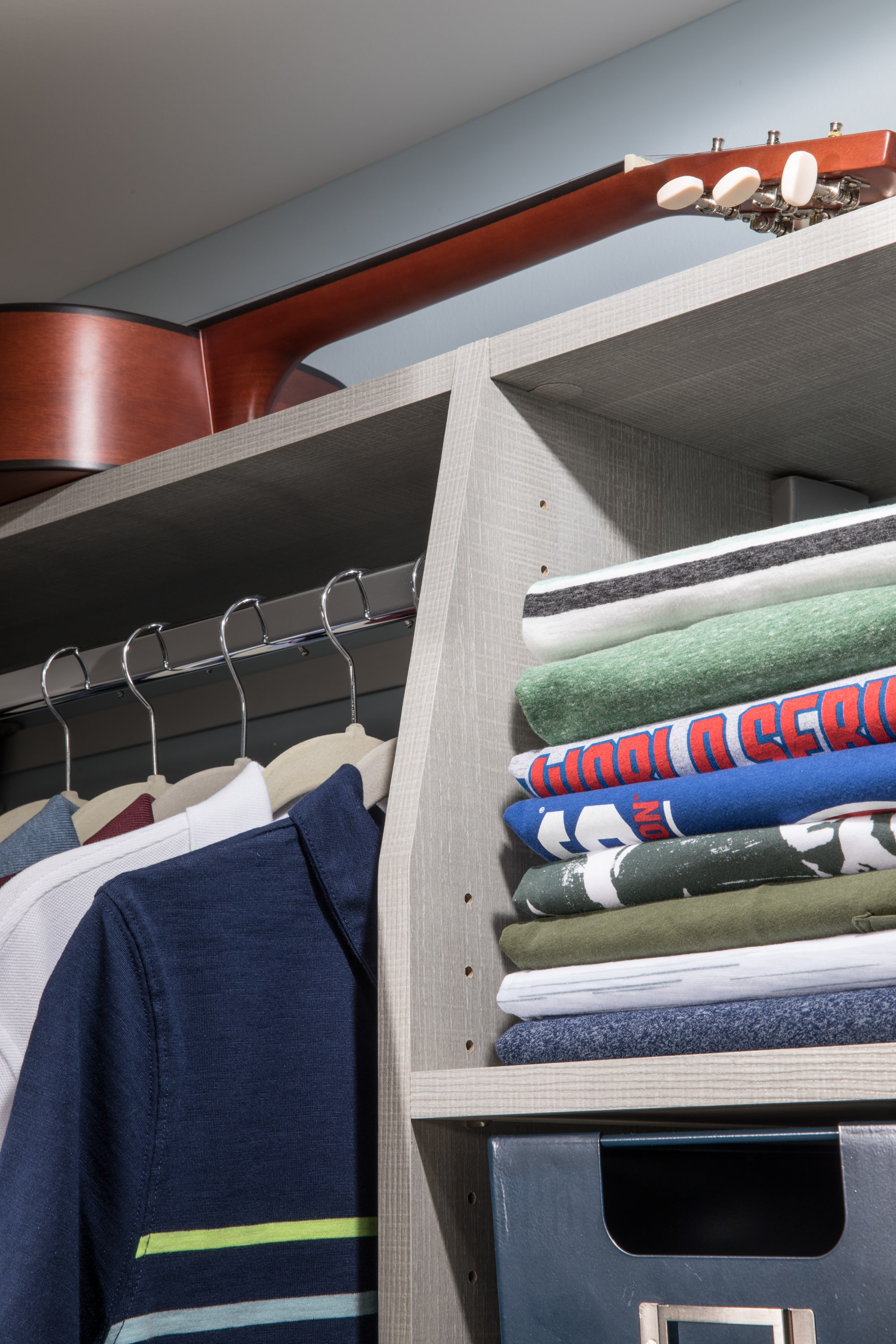 Shirts folded on shelves and hanging on racks with guitar on top