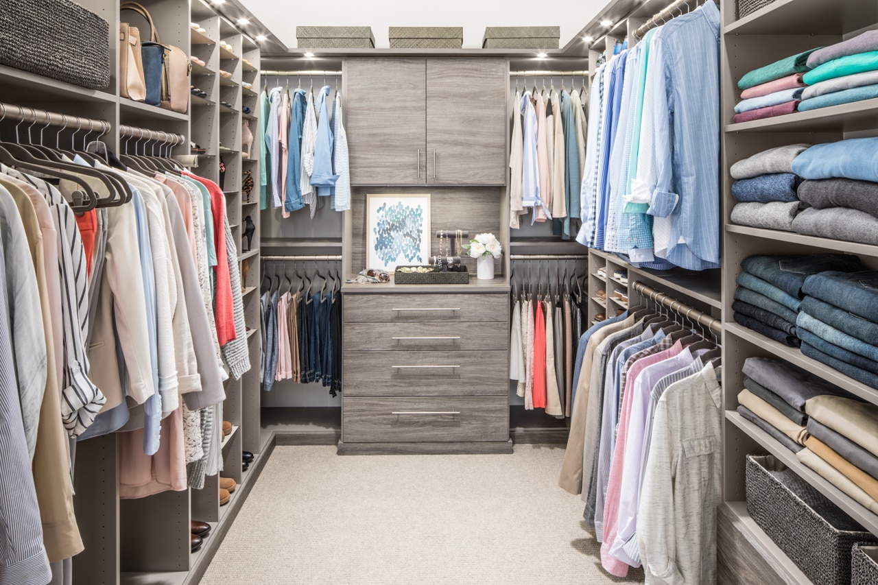 Walk in closet with clothing on hung on racks and placed on shelves on either side with a dresser at the end