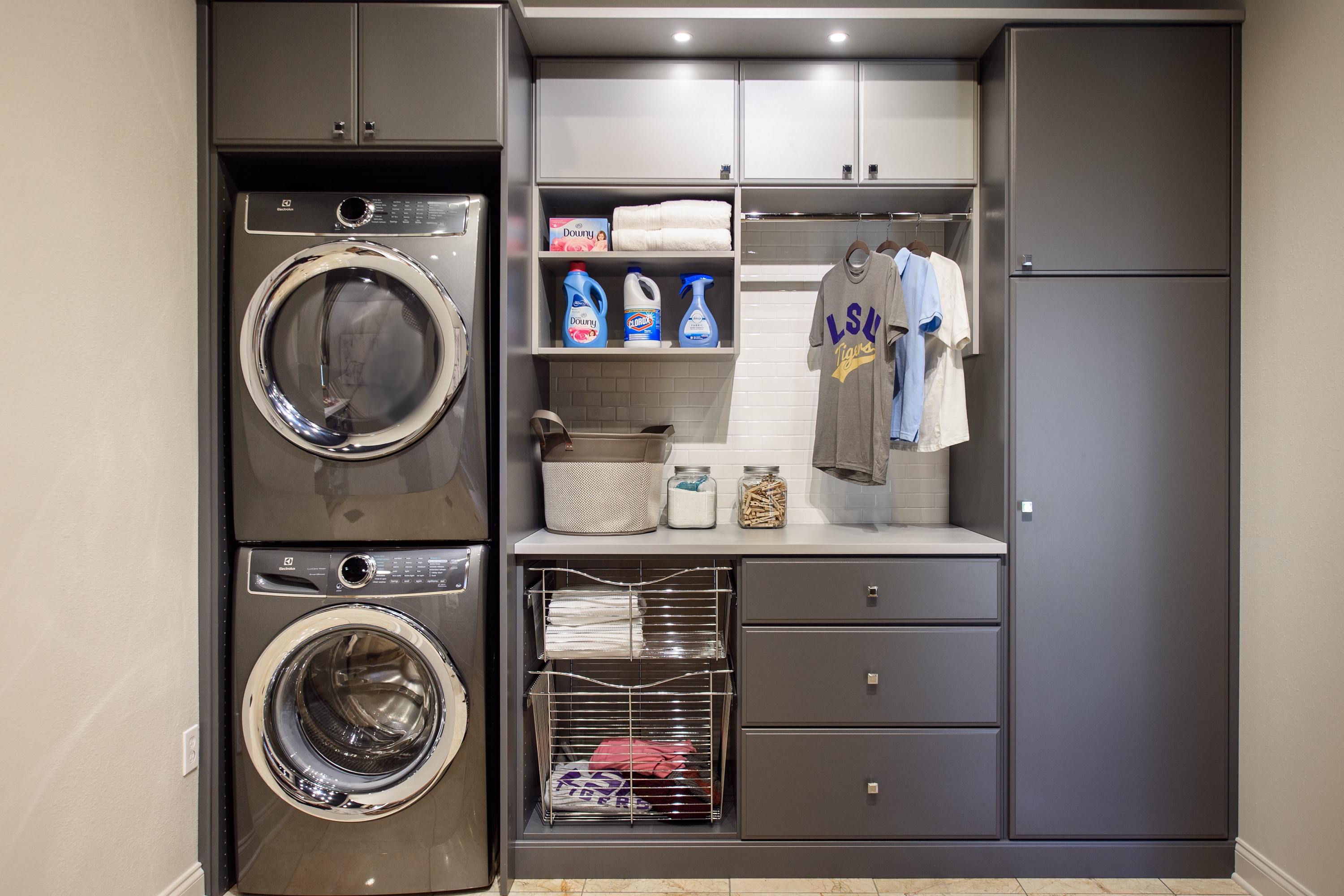 Laundry closet showing washer and dryer as well as clothing baskets, ironing board and shirts on rack