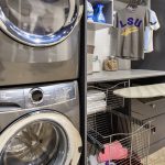 Laundry closet showing washer and dryer as well as clothing baskets, ironing board and shirts on rack