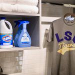 laundry closet with cleaning supplies on shelves and t shirts on rack