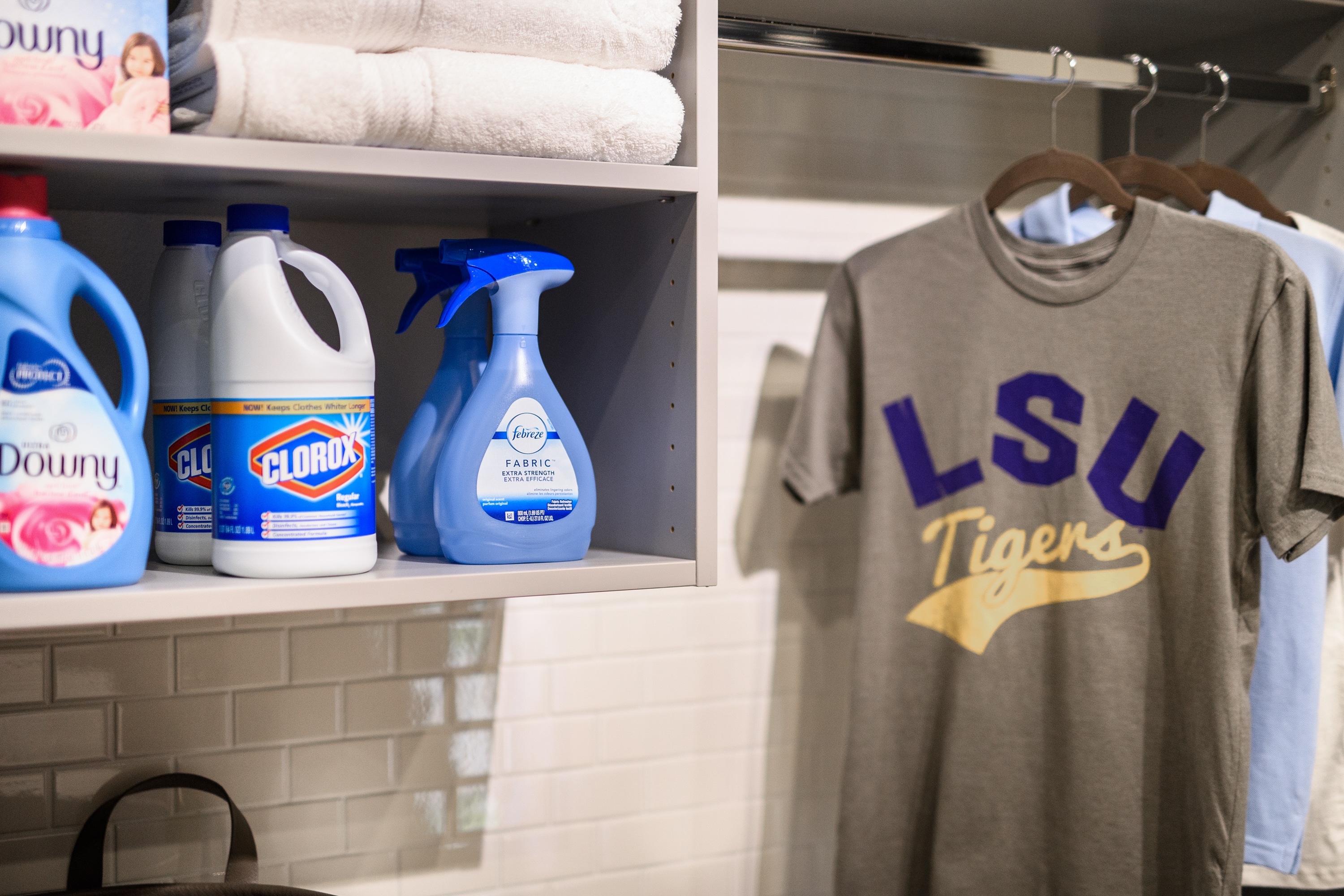 laundry closet with cleaning supplies on shelves and t shirts on rack